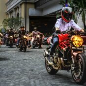A group of motorcyclists riding in formation on a cobblestone street in a city.